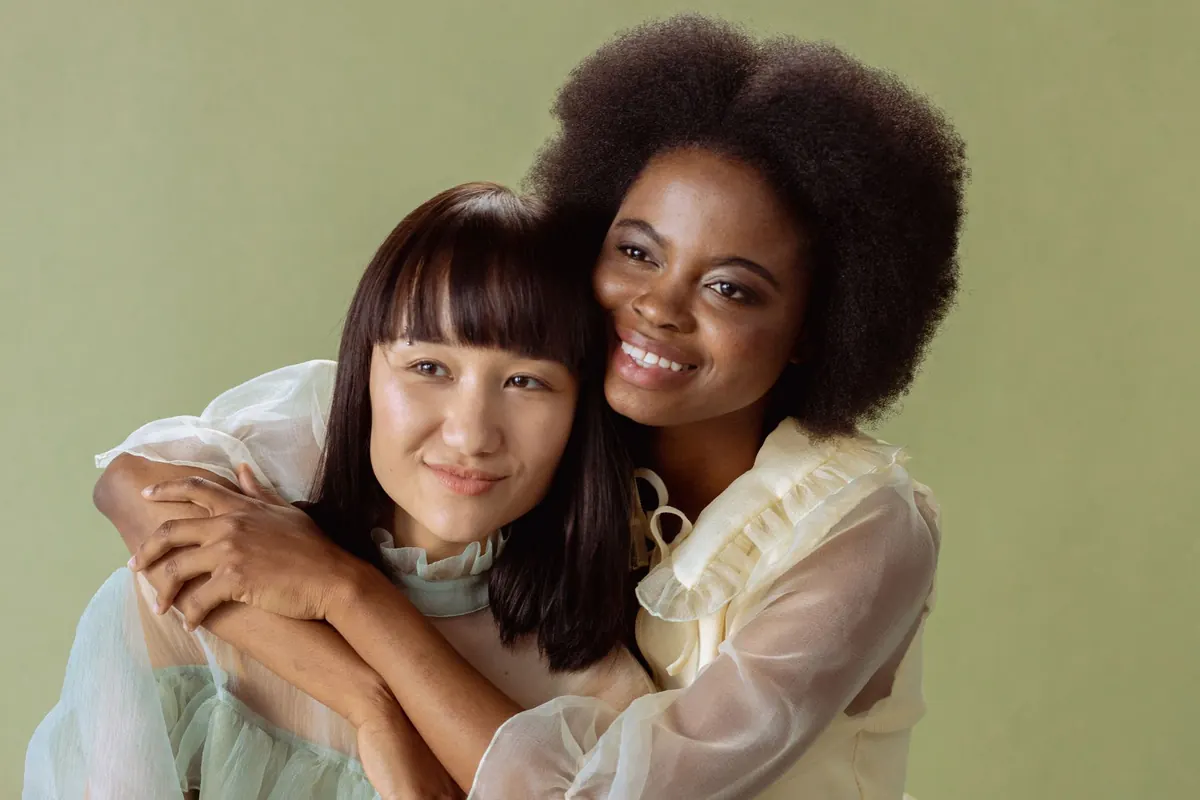 A joyful portrait of two diverse women embracing against a neutral background.