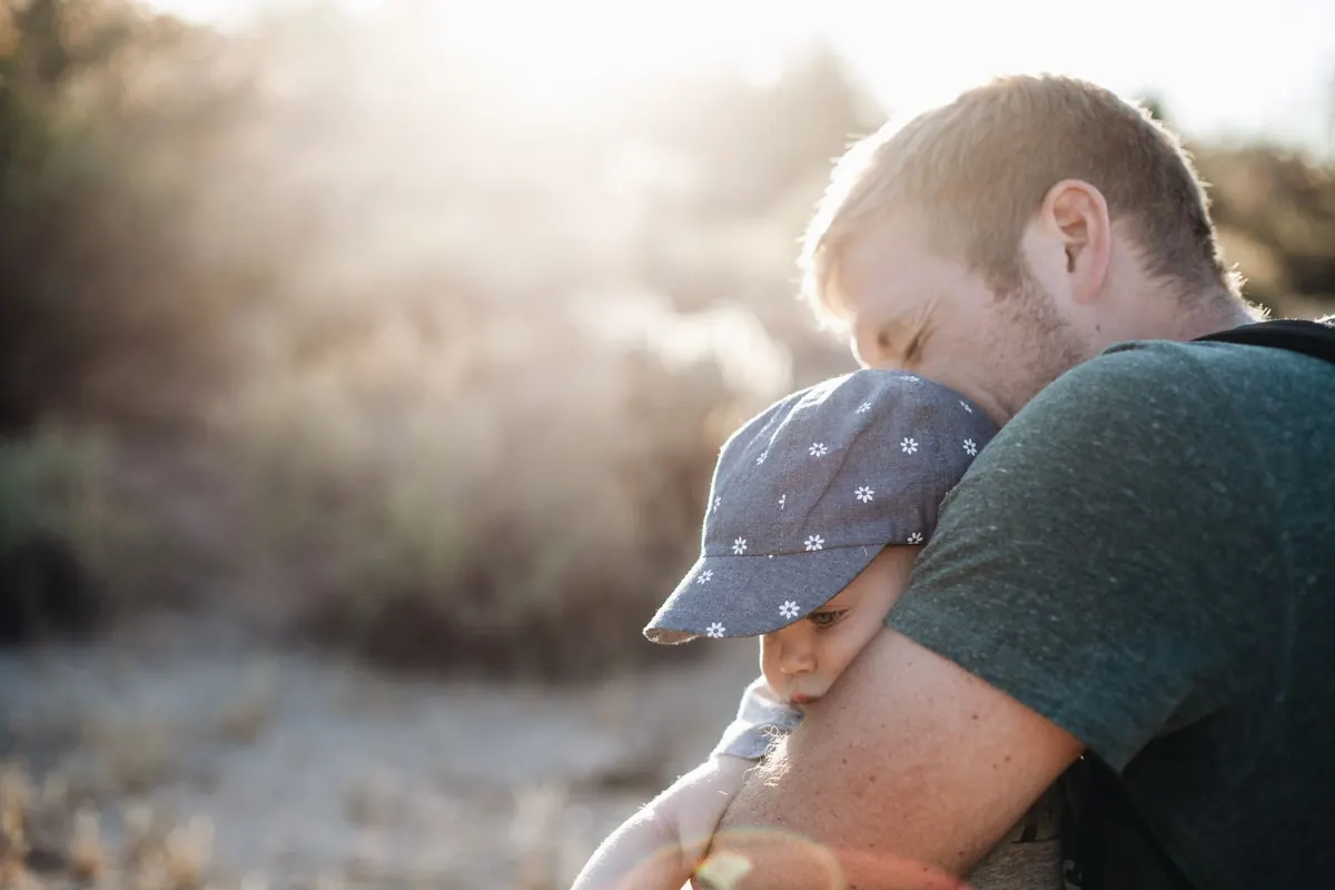 A father lovingly embraces his baby outdoors on a sunny day. Perfect for Father's Day themes.
