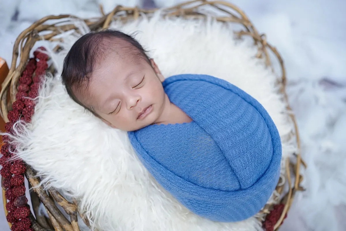 A serene newborn baby sleeping in a cozy blue swaddle, placed in a wicker basket.