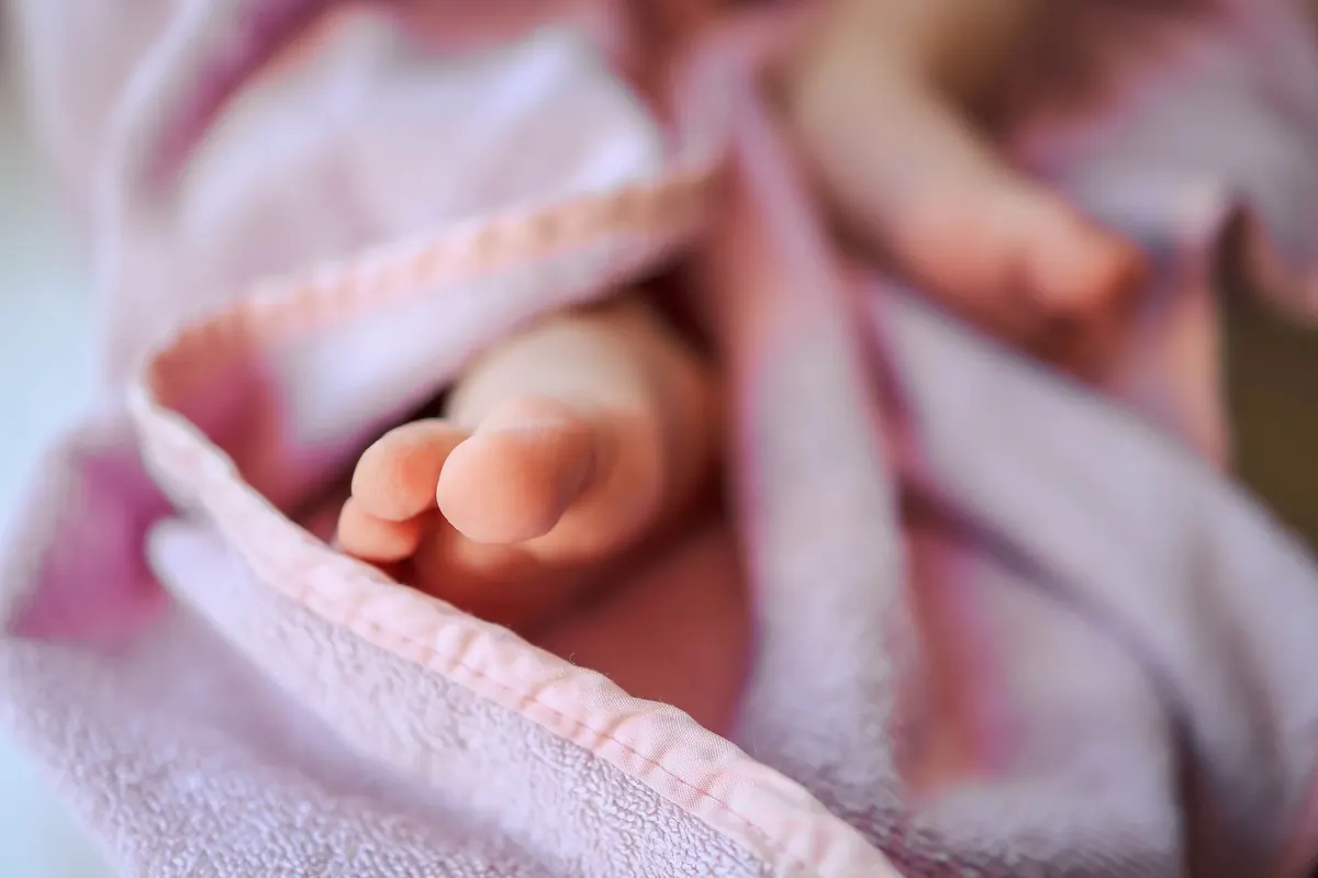 Tender close-up of baby feet wrapped in a soft pink blanket, captured with a blurred background.